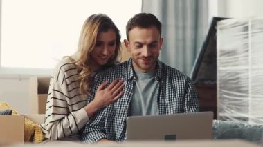 Bir çift, rahat ve davetkar bir yaşam alanıyla çevriliyken dizüstü bilgisayarlarıyla çok yakın bir şekilde otururlar.