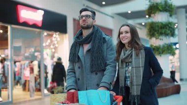 Noel hediyesi olan genç ve çekici bir çift alışveriş merkezinde gülümsüyor mutlu alışveriş yapan aile kadını Noel ağacı alışveriş mağazası hediyelik eşya dükkanında yavaş çekimde alışveriş yapıyor.