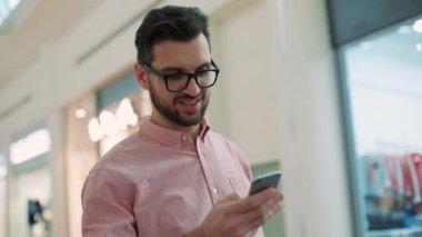 Gözlük takan yakışıklı genç adam telefon et. Saatine bak. Gülümse. Alışveriş merkezinde alışveriş yapan insan.
