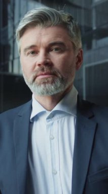 Modern ofisteki kameraya bakan çok yakışıklı orta yaşlı bir iş adamının portresi. Yakından, takım elbiseli, sakallı, yakışıklı, gri saçlı adamın görüntüleri. Yaşam tarzı, patron. Kendinden emin Kafkasyalı
