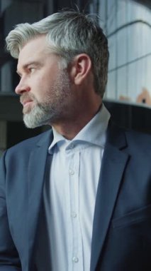 Düşünceli, yakışıklı, orta yaşlı, takım elbiseli bir adamın bakışlarını kaçırması. Şirketin gülümseyen CEO 'sunun yakın plan portresi doğrudan kameraya bakıyor. Gri saçlı iş adamı resmi giyinmiş. Kentsel