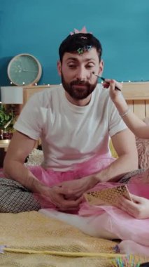 Bir erkek yatakta otururken bir kadın makyajını yapar, bir kız da katılır, neşe ve kahkaha getirir, özellikle de pembe etekli bir adamla.