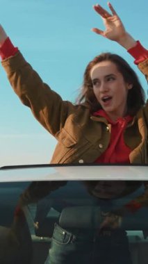 Kaygısız bir kadın, üzerinde canlı ve parlak bir mavi gökyüzü olan bir arabanın açık penceresinde neşeyle dans eder.