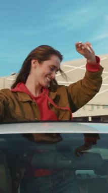 Neşeli bir kadın parlak, güneşli bir günün özgürlüğünü ve macerasını kucaklayan enerjik arabasından el sallıyor.