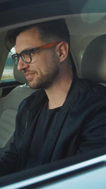 Şık gözlükleri olan kendine güvenen genç bir adam şık ve modern arabasıyla gezintiden zevk alıyor.