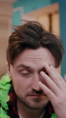 Yüzünde çok ciddi bir ifade olan bir adam renkli ve canlı bir çevrede canlı yeşil bir lei giyer.