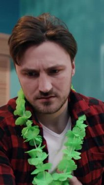 Flanel gömlekli ve yeşil kolyeli genç bir adam düşüncelere dalmış, karmaşık ve yankılanan duyguları ifade ediyor.