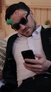 Güneş gözlüğü takan şık bir adam telefonuyla keyifli bir anın tadını çıkarıyor.