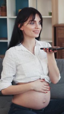 Neşeli, hamile bir kadın koltukta rahatça oturuyor, telefonda konuşurken ışıl ışıl gülümsüyor.