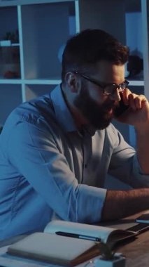 Gözlüklü sakallı bir adam cep telefonuyla konuşuyor ve modern iletişimi ön plana çıkaran profesyonel bir ortam sergiliyor.