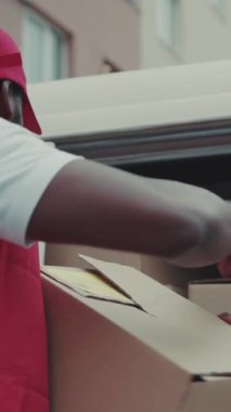 Kurye Afro-Amerikan genç adam kutusunu arabadan çıkardı ve mutlu bir şekilde gülümsedi. Karton teknoloji kutusu siparişi verdi. Posta cihazı, sakallı, lojistik postacı.