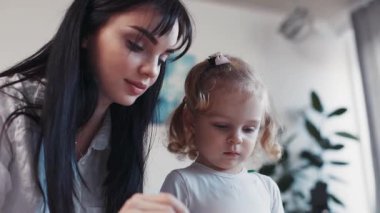 Kapalı yüzlü anne ve küçük kız birlikte kağıt boyuyor çocuk aile hobisi bebek sevecen kız ev boyacısı anne resim fırçası çocukluğu mutlu ev hanımı konuşma