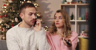 Aşık bir çift, hayran olunan Noel ağacının arka planında, koltukta oturuyor. Genç yakışıklı adam cep telefonuyla konuşuyor. Çekici kız TV kanallarını değiştiriyor.