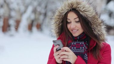 Kadın gülüyor ve telefonunda mesaj atıyor. Kız kış verandasında ve telefonu kullanıyor. Genç bir kadın, kış akşamı telefonuna mesaj atmaktansa kameraya gülüyor..