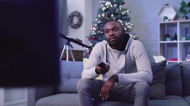 Pazar akşamı televizyon izleyen genç adam. Noel ağacının arka planında süsleri ve ışıkları olan ilginç bir programdan hoşlanan adam..