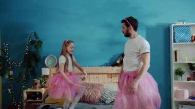 Evde eğlenceli bir kostüm partisi var. Mutlu genç aile babası ve kızı birlikte sihirli oyunlar oynuyorlar. Yakışıklı baba parmaklarının ucunda balerin gibi duruyor. Sevimli küçük kız gülüyor ve başını sallıyor.