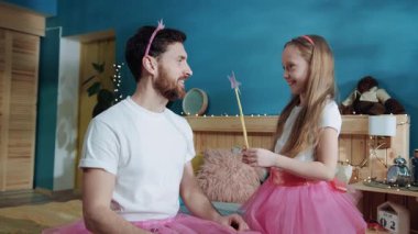 Pembe bir peri gibi giyinmiş, babasının üzerinde sihirli bir değnekle sallanan heyecanlı küçük bir kız. Yakışıklı genç adam babasının kızının sihirbazlık numaraları karşısında hayrete düşmüş. Evde sihir.