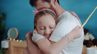 Evde güzel, genç bir aile kucaklaşması. Küçük mutlu kız, babasını kucaklıyor, gülümsüyor ve tatilde iyi vakit geçiriyor..