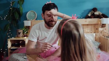 Küçük güzel kız, babasının yüzüne göz farı sürerek parti için onu giydiriyor. Baba ve kızı birlikte doğum günü kutlaması için hazırlanıyorlar. Makyaj.