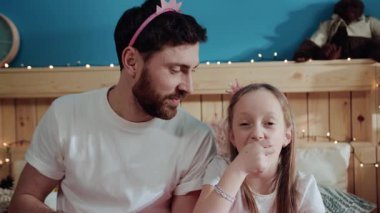 Yakışıklı genç baba ve güzel kızının portresi. Patlamış mısırı kameraya atarken birlikte gülüyorlar. Yatakta otururken..