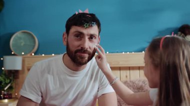 Üzgün bir ifadeyle yardım isteyen zavallı bir babanın portresi. Mutlu kızın, babasının yüzüne makyaj yaparken yan görünümü. Eğlenceli yetiştirilme. Doğum günü partisi.