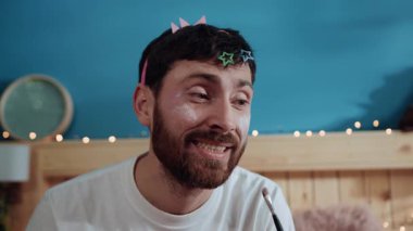 Zavallı, sıkkın, genç baba kameraya bakıp gülümsüyor. Yakından komik bir kız, süslü kostüm partisinde babasına makyaj yapıyor..