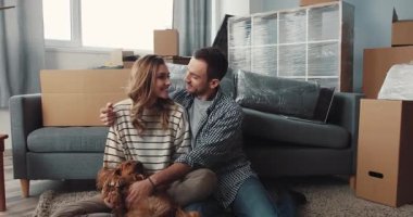 Mutlu bir çift yeni evlerinde mutlu mesut eğleniyor. Etrafı kutularla çevrili.