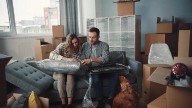 Bir çift mutlu bir şekilde yeni evlerinde sevgili köpekleriyle birlikte kutuları açıyor ve erzakları taşıyorlar.