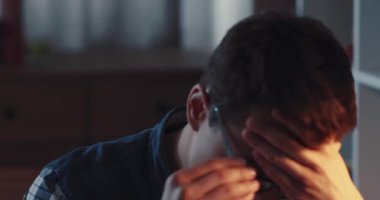 Gözlüklü düşünceli bir genç adam, kapalı bir etkinlikte çalışırken derin bir şekilde yansıtıyor.