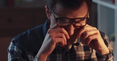 Gözlük takan ve ekose gömlek giyen genç bir adam, kapalı bir alanda derin bir konsantrasyon gösterir