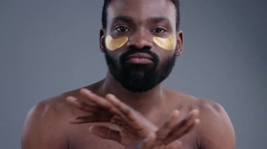 Gri arka planda altın göz bantları takarak komik bir Afrika dansı yapan kendinden emin, çıplak zenci adamın yakın çekimi..