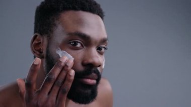 Kameraya bakarak yüzüne nemlendirici krem süren yakışıklı, genç ve seksi bir adam. Çekici bir adamın çıplak portresi. Cildine önem veriyor. Bir güne hazırlanıyor..