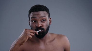 Yakışıklı, atletik, üstsüz, dişlerini fırçalayan, arka planda izole edilmiş aynaya bakan Afro-Amerikalı adam. Sağlıklı günlük rutin kavramı.