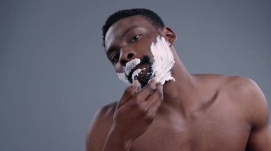 Çekici, kibar, siyah erkek model, aynaya bakarak yüzüne tıraş kremi sürüyor. Banyoda tıraş olan seksi kaslı Afrikalı adamın yakın çekimi. Günlük rutin kavram.