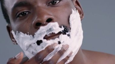 Yakışıklı, Afro-Amerikan tişörtsüz, tıraş olan ve yüzüne krem süren genç adamın yakın çekimi. Tıraş köpüğüyle kaplı erkek modelin portresi..
