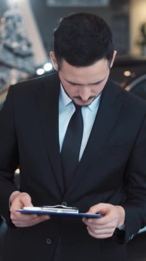 Resmi takım elbiseli yetenekli bir profesyonel, bir araba galerisinde önemli belgeleri dikkatle inceliyor.