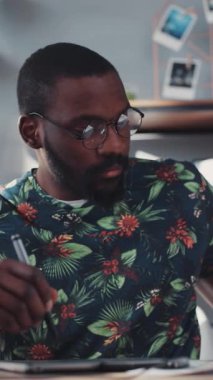 Parlak çiçekli bir kazak giyen bir adam masasında yaratıcı bir işe dalmış, dikkatle odaklanmış.