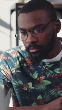 Şık gözlüklü genç bir adam şık bir dizüstü bilgisayarla çalışıyor. Göze çarpan çiçekli bir süveteri var.