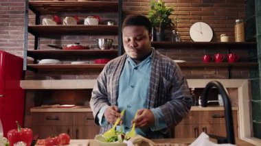 Neşeli bir adam, modern bir mutfakta taze salata yapmaktan, sağlıklı yemek pişirmekten ve yaşam tarzı seçimlerinden zevk alır.