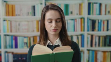 Kendini işine adamış genç bir kadın etrafını sayısız kitaplıkla çevrili bir şekilde kitap okumaya dalmış.