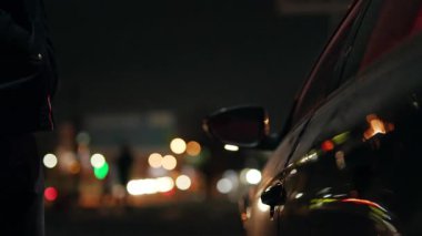 Bu görüntü, bir araba ve uzak bir siluetin yer aldığı kasvetli bir şehir gece sahnesini yakalıyor.