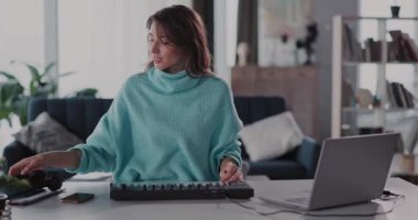 Rahat bir süveter giymiş genç bir kadın şık ofis ortamında özenle bir dizüstü bilgisayar üzerinde çalışıyor.