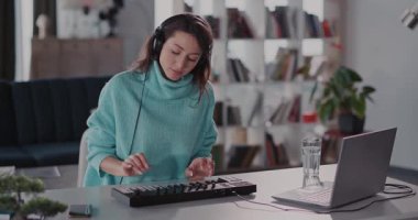 Bitkiler ve kitaplarla dolu modern bir ev ofisin klavyesine özenle yazı yazan odaklanmış ve kendini işine adamış bir kadın.