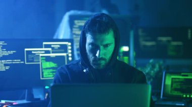 Birden fazla bilgisayar ekranı ile dolu loş bir odada, odaklanmış bir hacker akış kodu arasında özenle çalışır