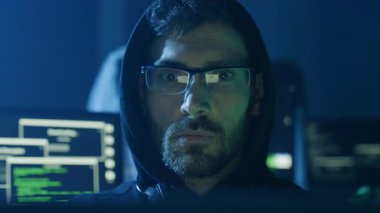 Şık bir kapüşonlu kararlı bir kişi loş bir odada gelişmiş siber güvenlik çözümleri üzerinde çalışıyor.