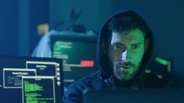 Kendini işine adamış bir hacker, loş aydınlatılmış bir odadaki çoklu ekranlardaki verileri etkili bir şekilde kodluyor ve titizlikle analiz ediyor.