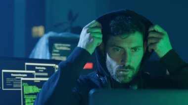 Becerikli ve odaklanmış bir hacker, loş bir çalışma alanındaki çift ekran verilerini derinden analiz ediyor.