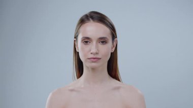 Sakin bir kadın doğal güzelliğini ve duruşunu sergileyerek tarafsız bir arkaplanda zarif bir şekilde durur.