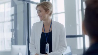 Modern bir ofiste, beyaz takım elbiseli profesyonel bir kadın beyaz tahtada fikirlerini sunar, erkek bir meslektaşla yakınlaşır, takım çalışması sergiler.