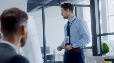 Profesyonel bir ofiste, mavi gömlekli ve kravatlı bir adam küçük bir seyirciye etkili iletişim ve takım çalışması sergileyen bir sunum sunar.